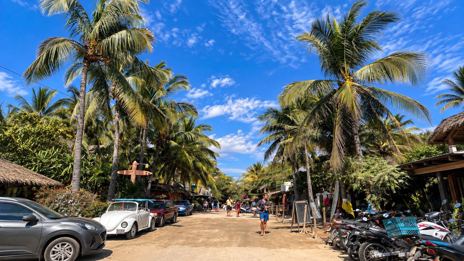 Eine Straße in Zicatela, Puerto Escondido, mit Palmen, Autos und Motorrädern